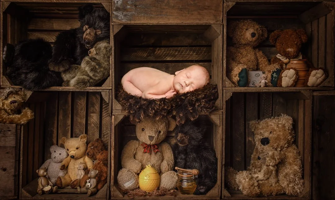 a newborn sleeping among crates of teddy bears - digital image