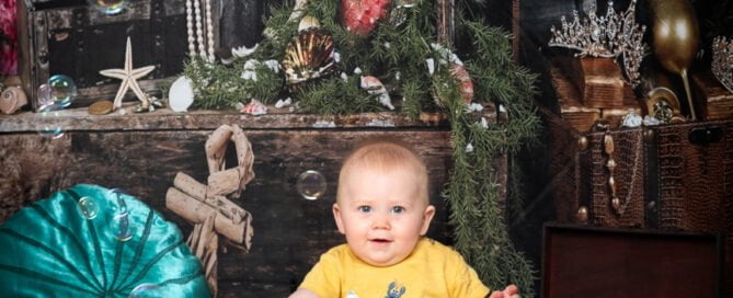 a baby posing in an underwater scene set up in a photographic studio with a backdrop and plush props