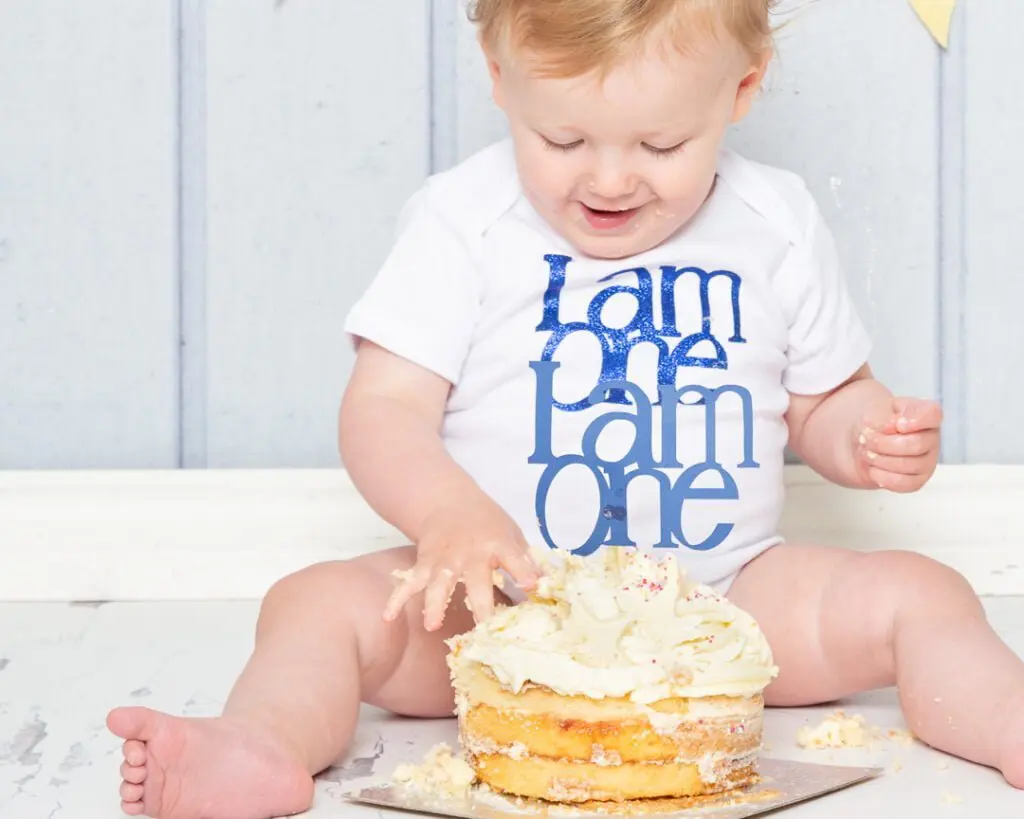 Cake Smash Photo Shoots in East Grinstead West Sussex a little boy in a vest that says 'i am one' at a cake smash photo shoot