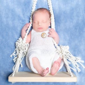 a sleeping newborn posed on a white swing at a photo shoot