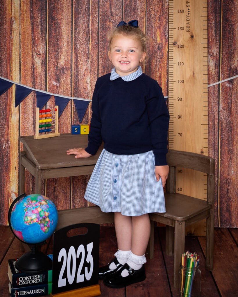 a little girl poses in her new school uniform in a school themed set in my studio