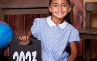 a little girl poses with a sign saying 2023 at a school themed photo shoot