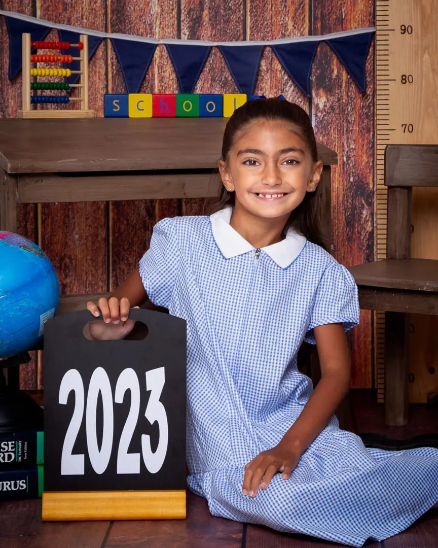 a little girl poses with a sign saying 2023 at a school themed photo shoot