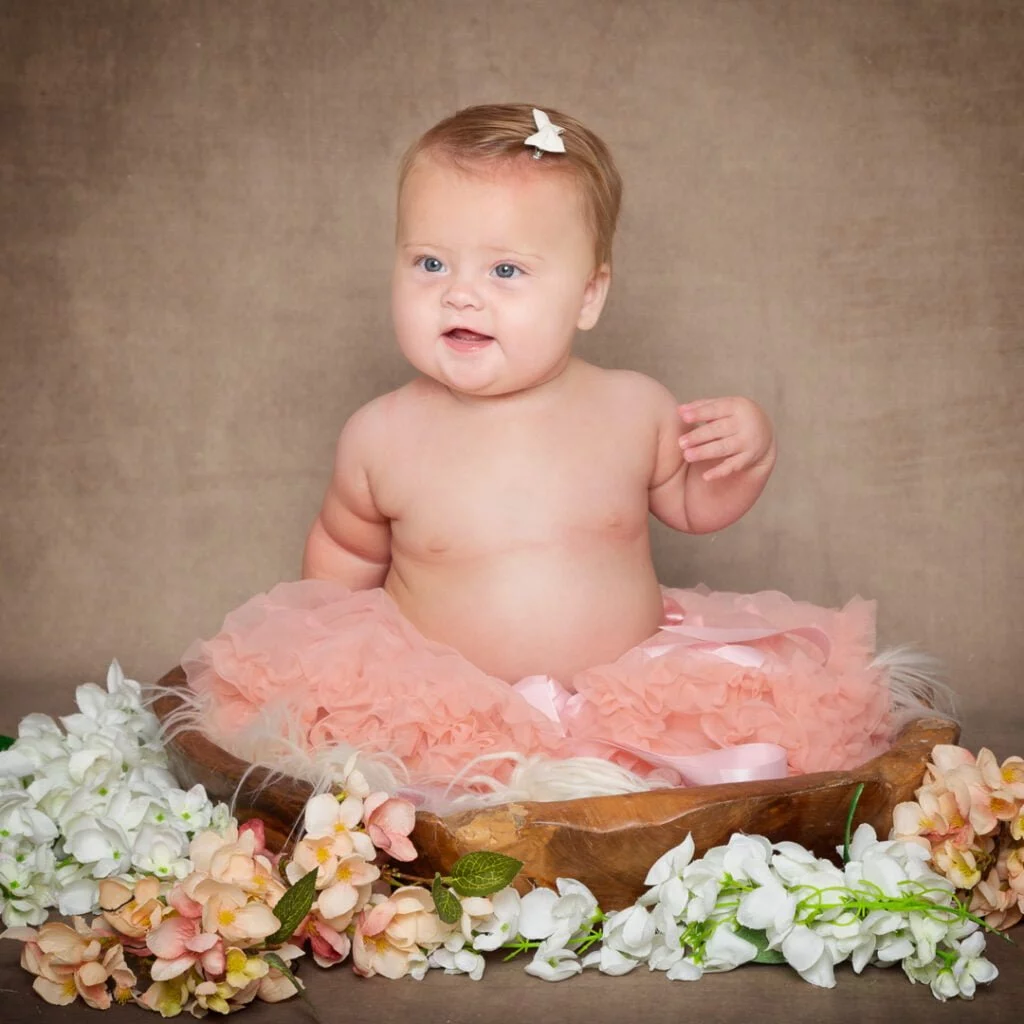 a baby in a peach pettiskirt poses in a brown wood bowl