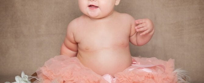 a baby in a peach pettiskirt poses in a brown wood bowl