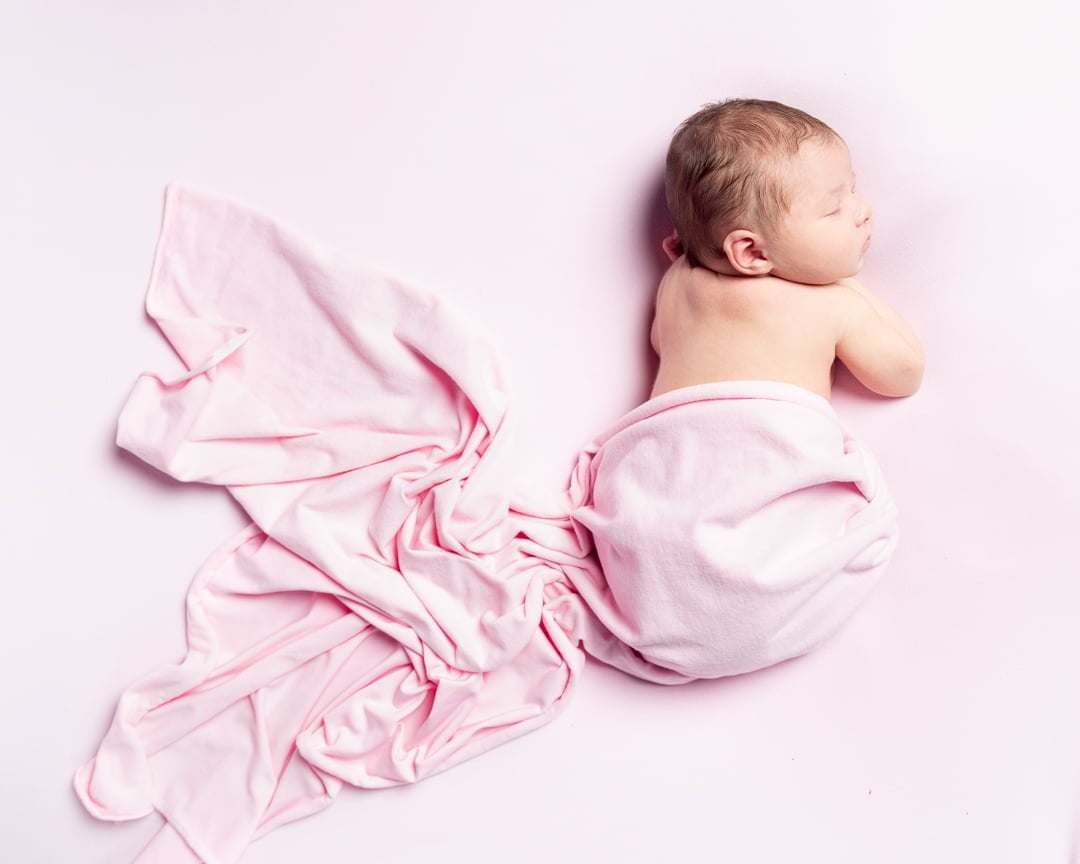 a newborn baby girl sleeping with a trailing pink wrap