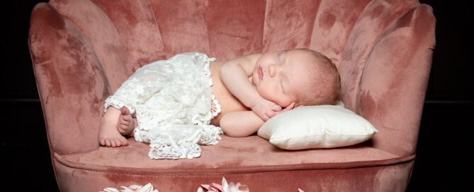 a newborn with a lace wrap sleeping in a small pink chair