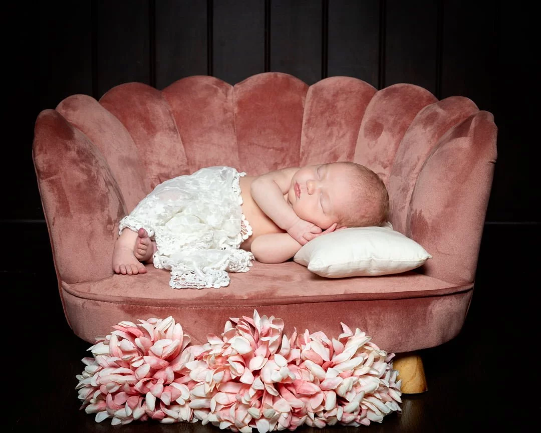 a newborn with a lace wrap sleeping in a small pink chair