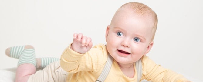 a baby poses on their tummy waving at the camera