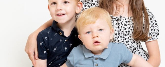 Three siblings posing for a photo against a white studio background