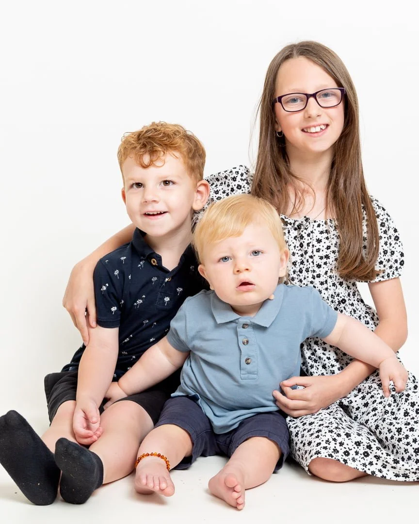 Three siblings posing for a photo against a white studio background