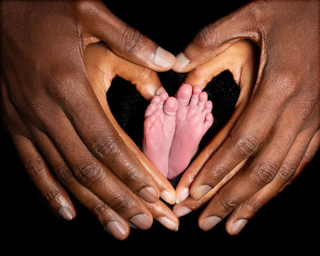 a newborn's feet surrounded by its parents hands in a heart shape