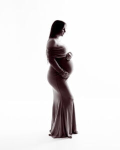 A black and white image of a pregnant woman posing in profile against a white background and professional pregnancy photo shoot