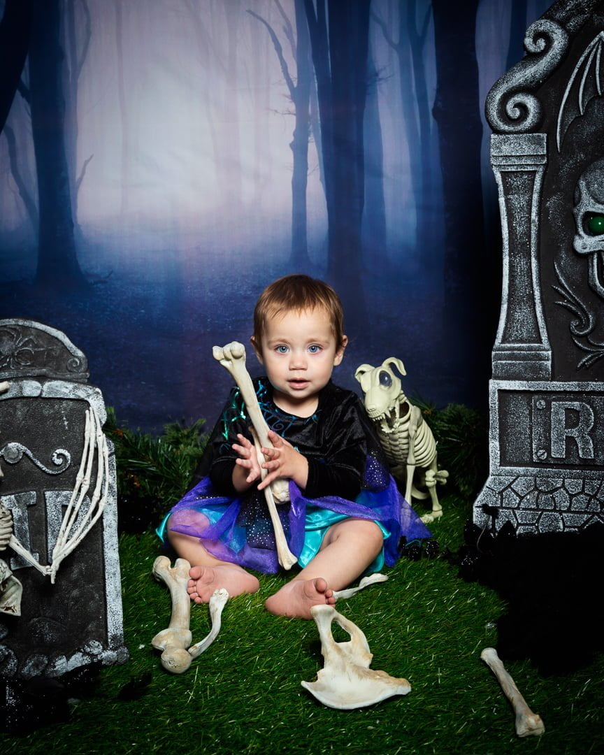 a little girl poses with a fake bone at a graveyard themed Halloween photo shoot