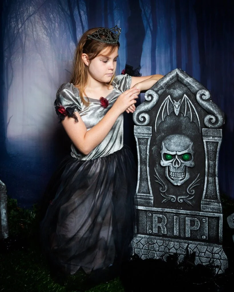 a little girl poses with a gravestone graveyard themed Halloween photo shoot