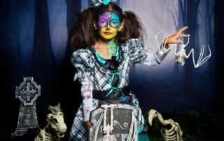 a little girl in spooky face paint poses at a halloween themed photo shoot in a graveyard set