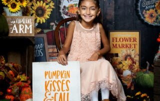 a little girl poses in a pumpkin and sunflower themed photo shoot set