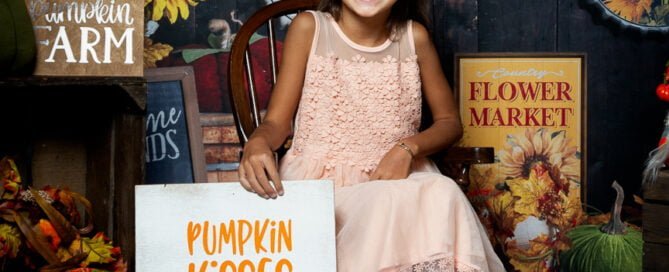 a little girl poses in a pumpkin and sunflower themed photo shoot set