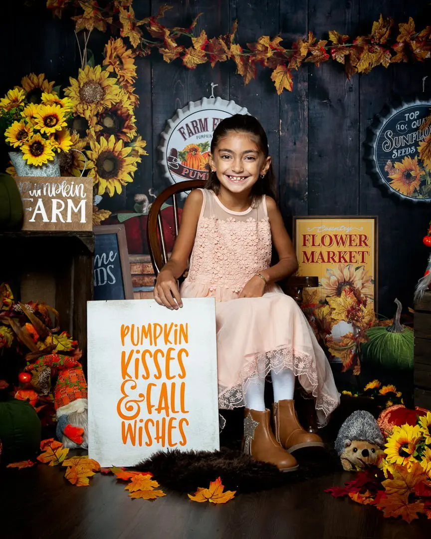 a little girl poses in a pumpkin and sunflower themed photo shoot set
