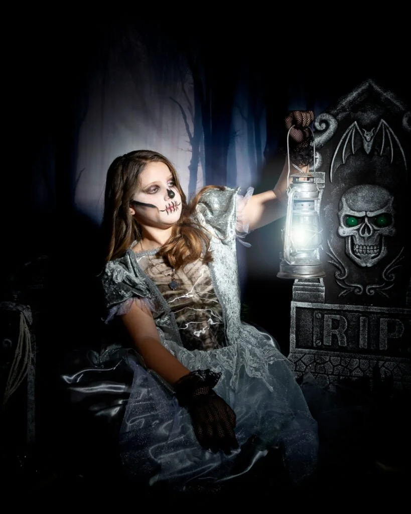 a little girl holds a lanterns in a graveyard themed Halloween photo shoot