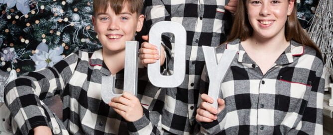 three older children wear matchign christmas pjs and pose for a christmas photos in a fireplace scene set