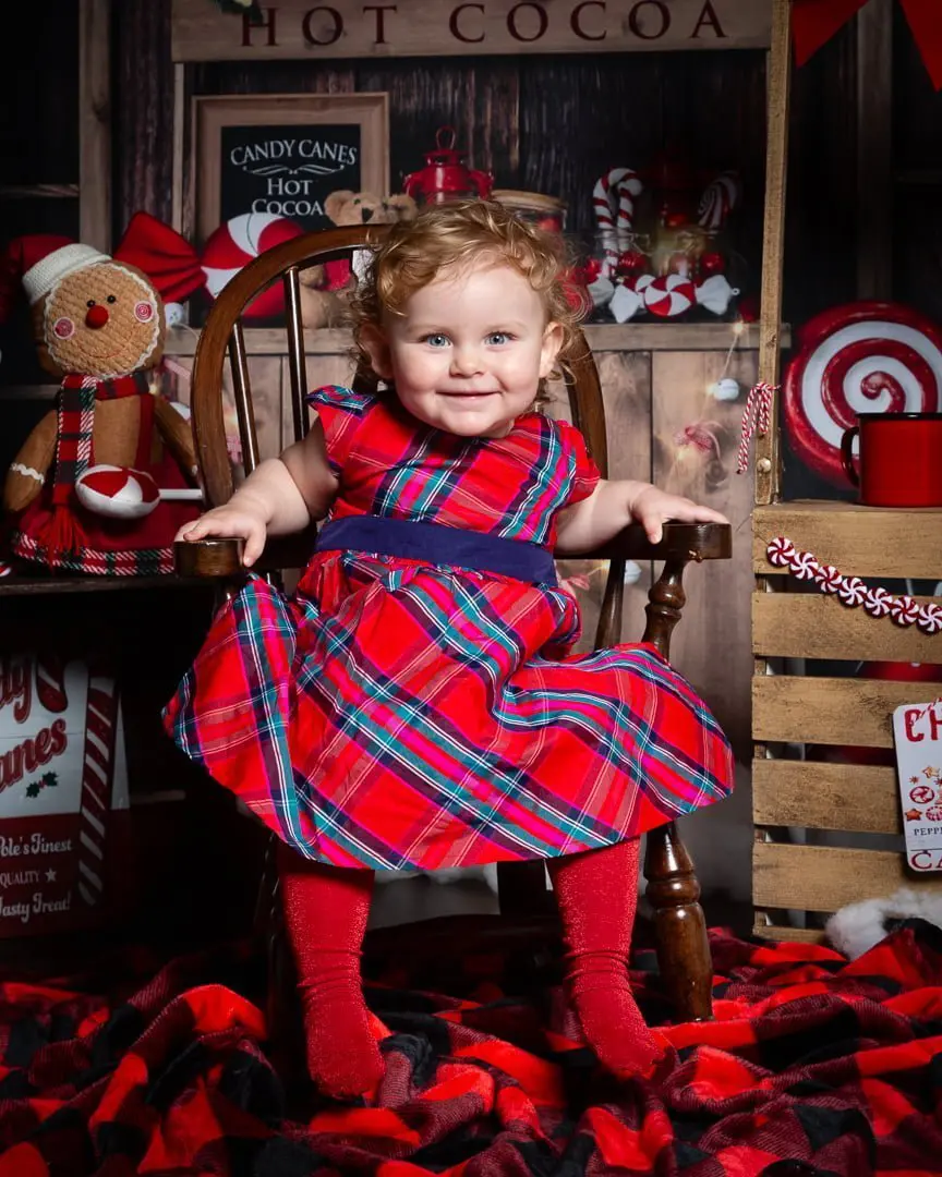 a little girl in a tartan dress sits in a cocoa stand photo shoot mini set
