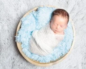 a newborn sleeping in a bowl filled with blue fluff
