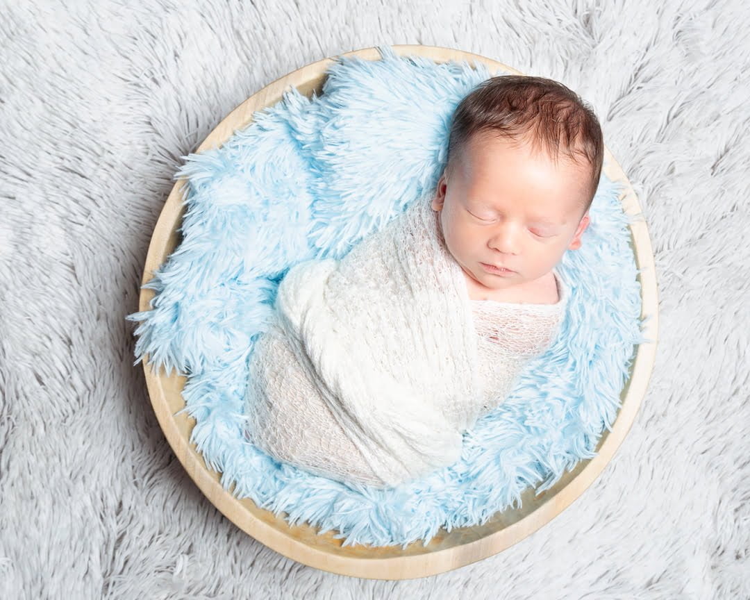 a newborn sleeping in a bowl filled with blue fluff