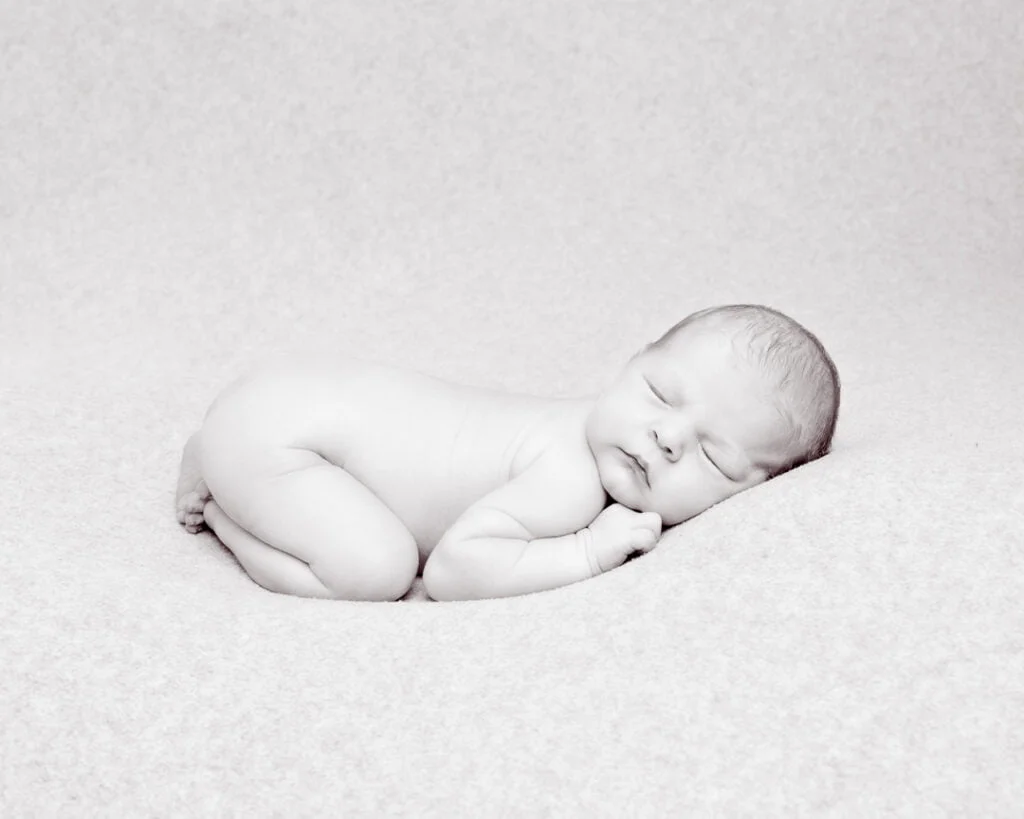 a black and white image of a newborn in a classic newborn tummy tuck pose