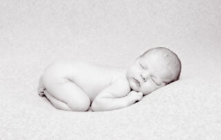 a black and white image of a newborn in a classic newborn tummy tuck pose