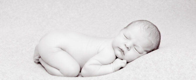 a black and white image of a newborn in a classic newborn tummy tuck pose