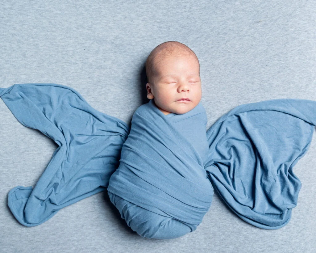 a newborn wrapped in a blue cloth with the ends pulled out to look like butterfly wings