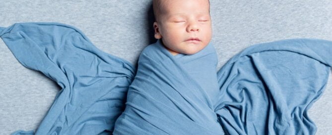 a newborn wrapped in a blue cloth with the ends pulled out to look like butterfly wings