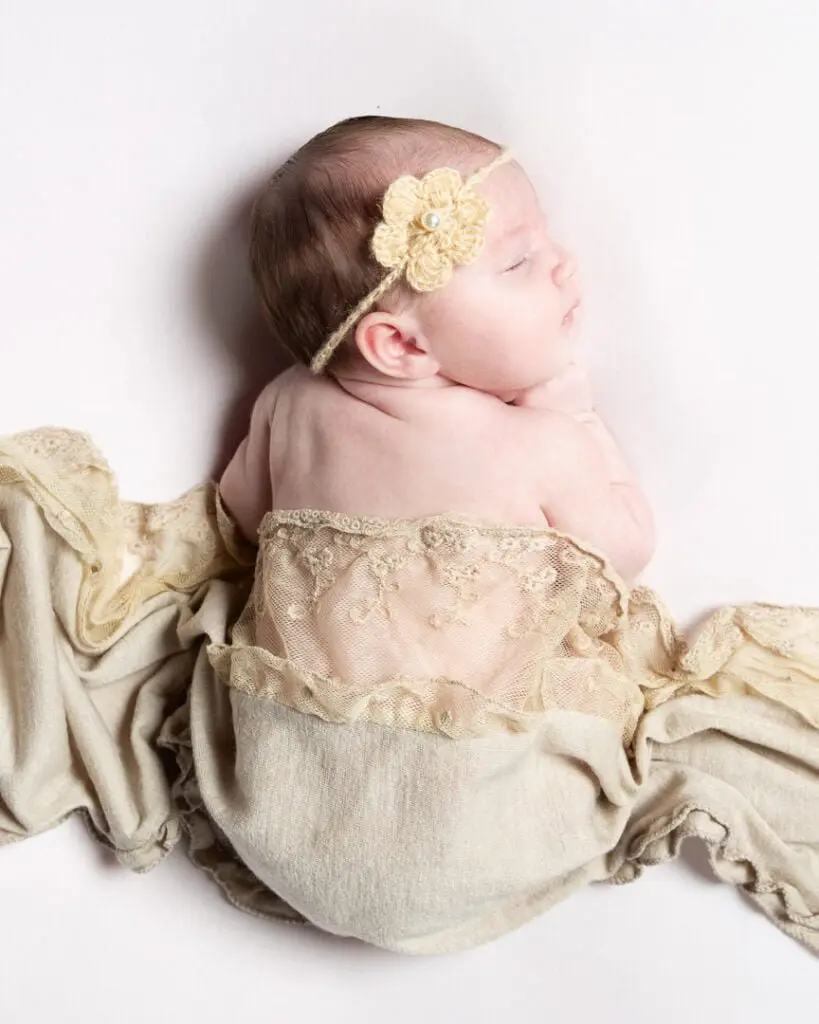 Newborn Photography in East Grinstead a sleeping newborn wrapped in neutral shades and lace fabrics