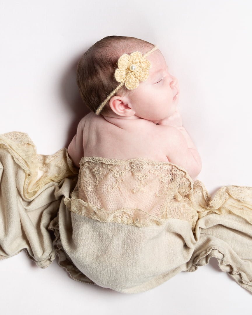 a sleeping newborn wrapped in neutral shades and lace fabrics