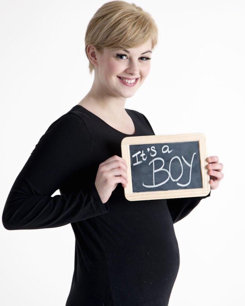 a pregnant girl poses with a sign reading it's a boy