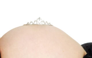 A pregnancy belly photographed with the mother lying down on her back, with a diamond tiara on top of the bump