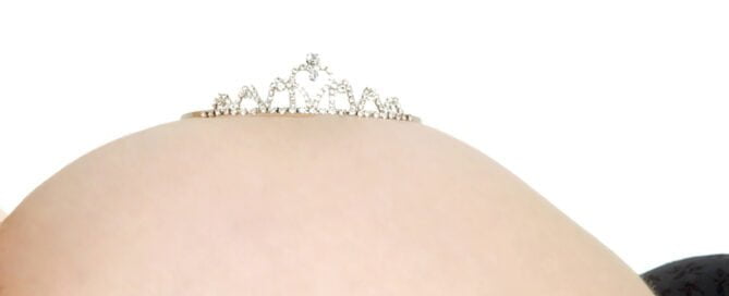 A pregnancy belly photographed with the mother lying down on her back, with a diamond tiara on top of the bump