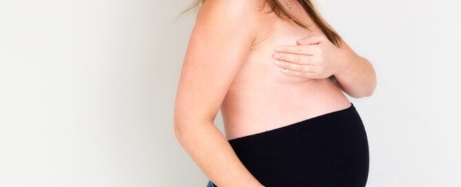 a woman poses in her maternity jeans looking down to her bump