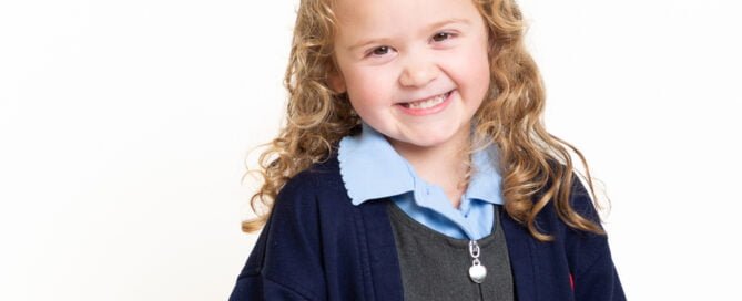 a little girl poses against a white background in her school uniform for a studio school portrait