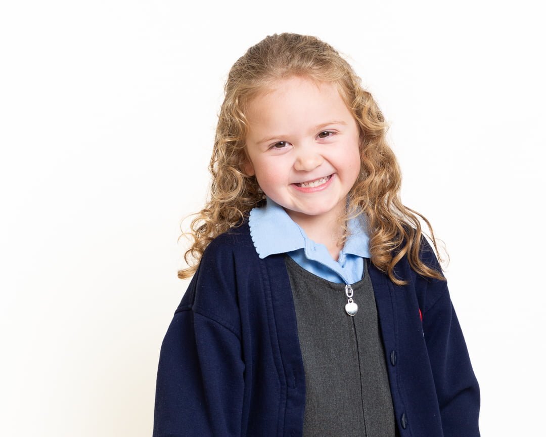 a little girl poses against a white background in her school uniform for a studio school portrait
