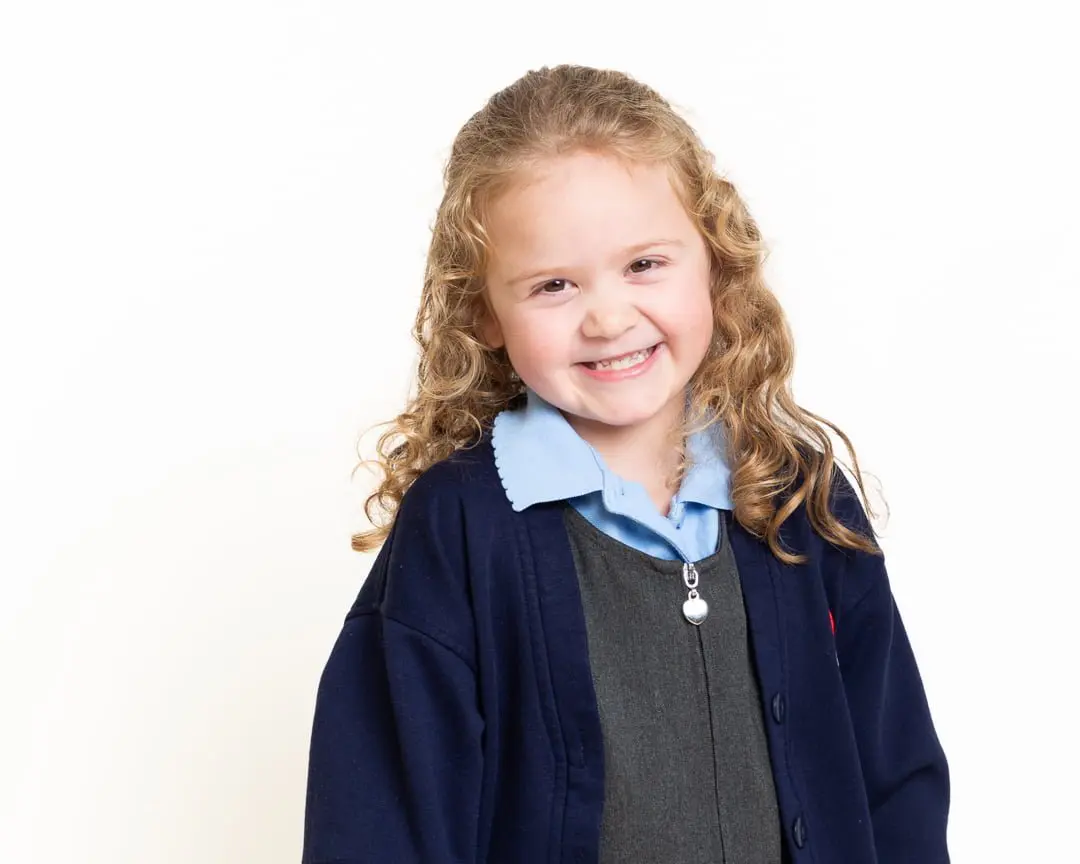 a little girl poses against a white background in her school uniform for a studio school portrait