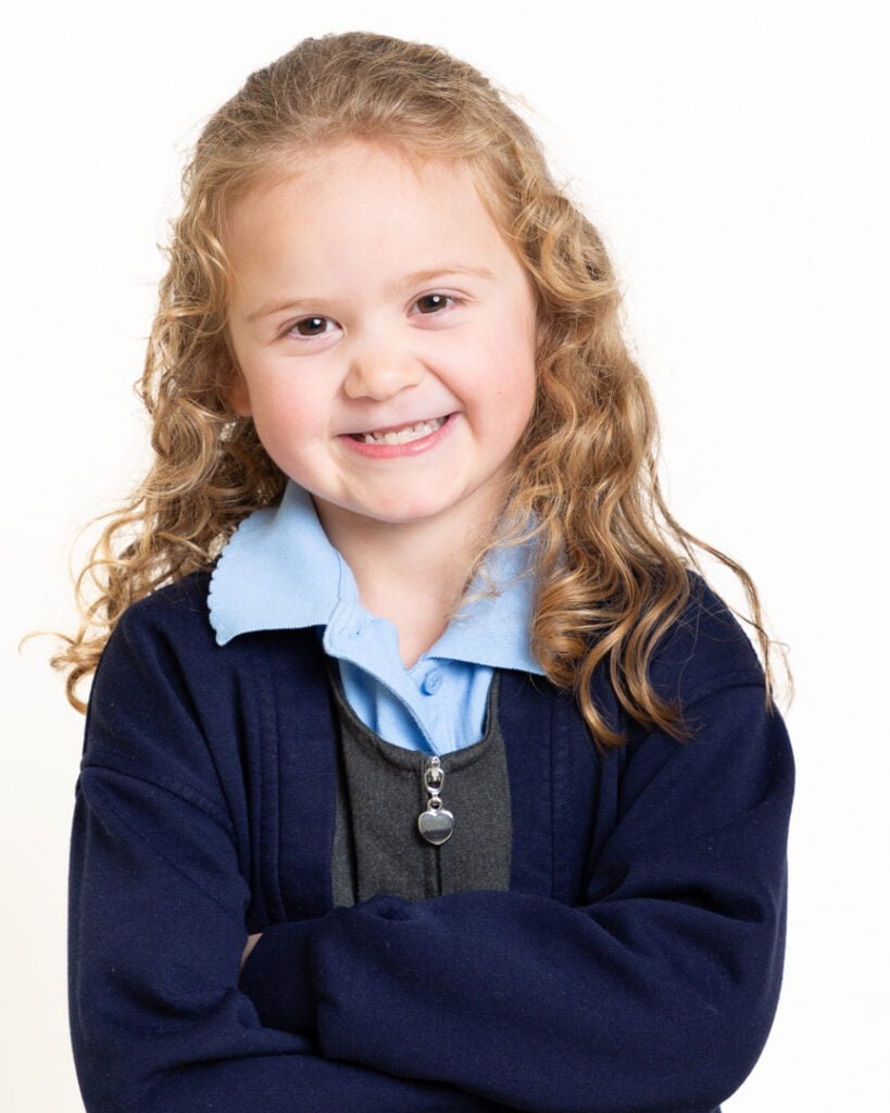 a little girl smiling for the camera dressed in her new school uniform against a white background