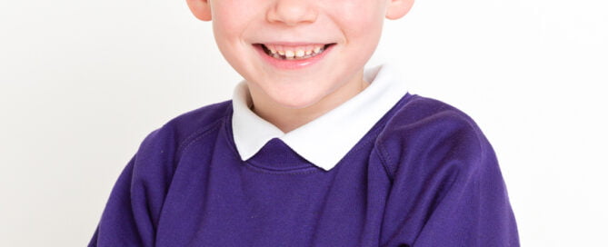 a little boy poses against his white background in his new school uniform at a school photo shoot in my studio
