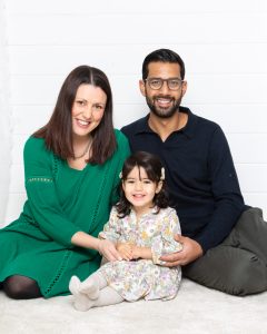 A family of two parents and a little girl sit on the floor against a white background for a professional family portrait photo shoot.