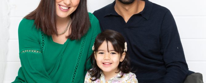 a mum and dad sit on the floor with their daughter for a professional family portrait
