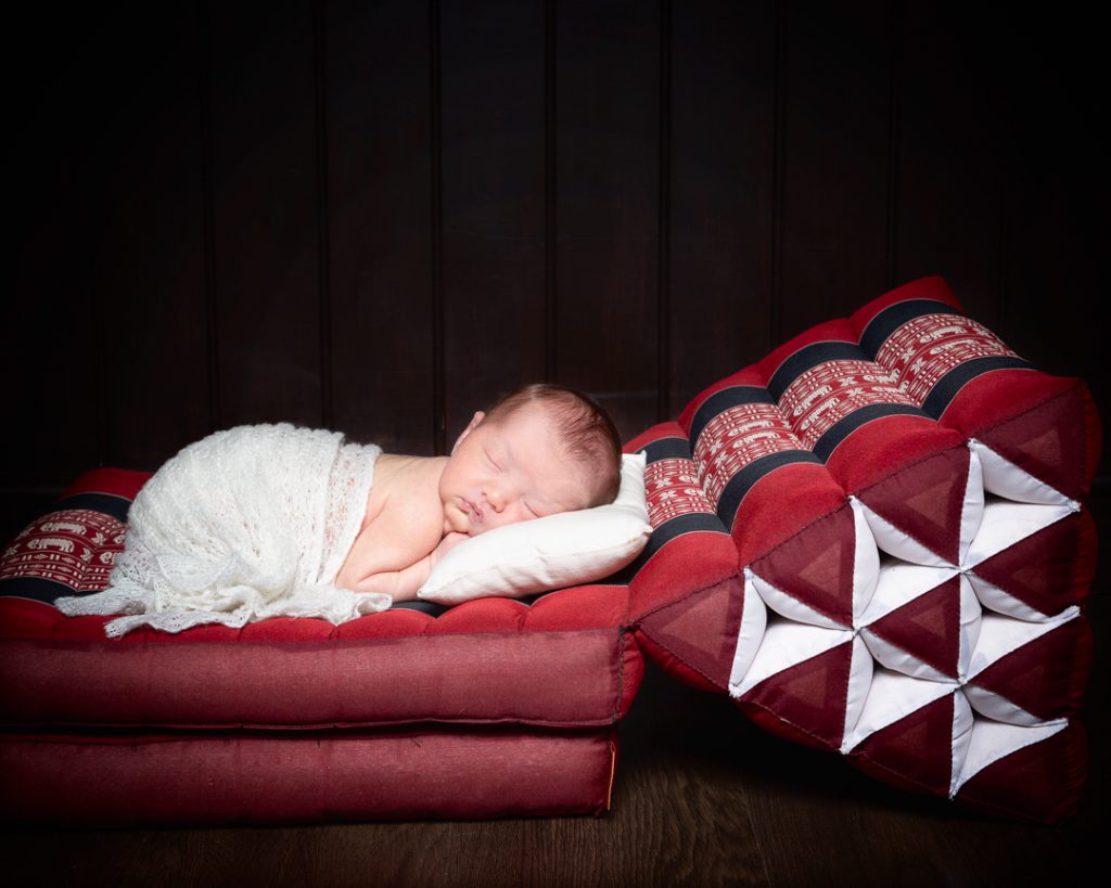 a newborn sleeping wrapped in white on a Thai bed mat from a client's holiday