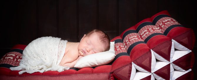 a newborn sleeping wrapped in white on a Thai bed mat from a client's holiday