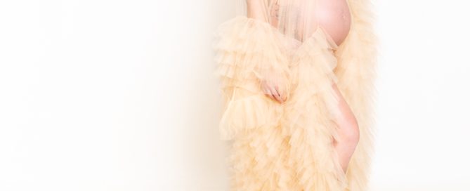 a pregnant lady poses for a photo in a dramatic cream tulle robe
