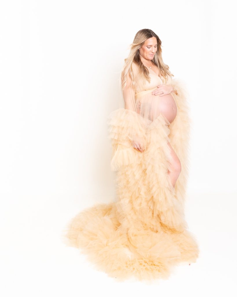 a pregnant lady poses for a photo in a dramatic cream tulle robe